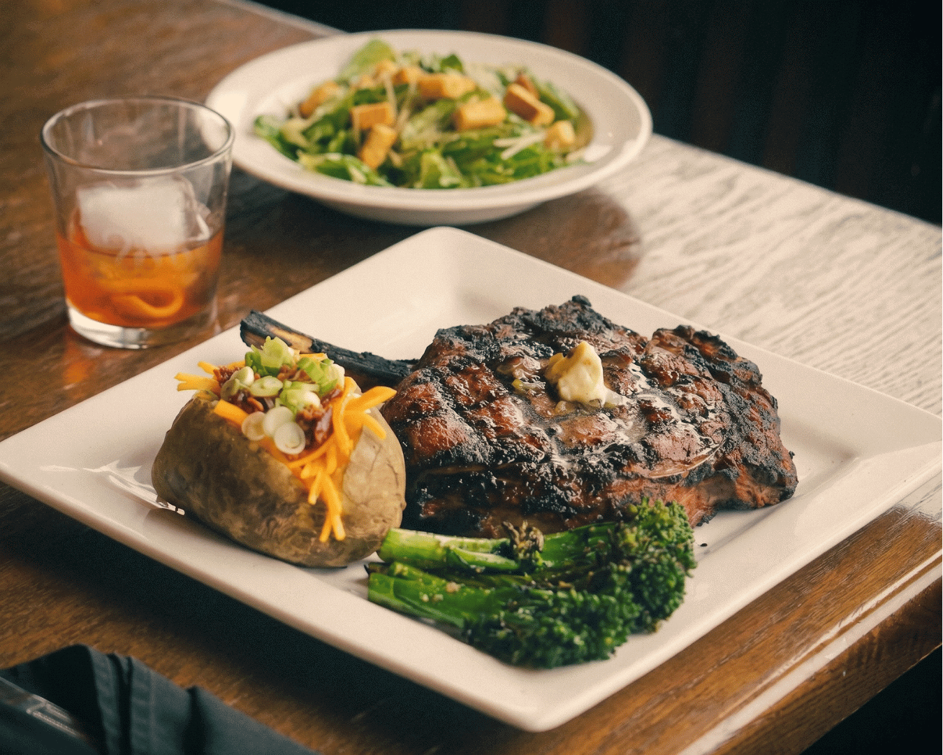 Grilled steak with baked potato, asparagus, and side salad on a white plate.