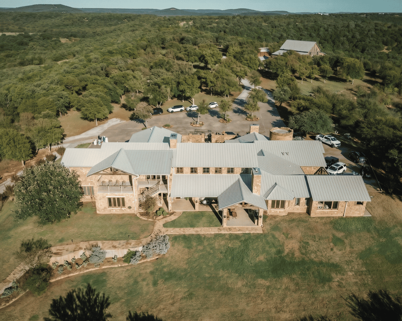 Aerial view of a large ranch-style property with multiple buildings and surrounding greenery.