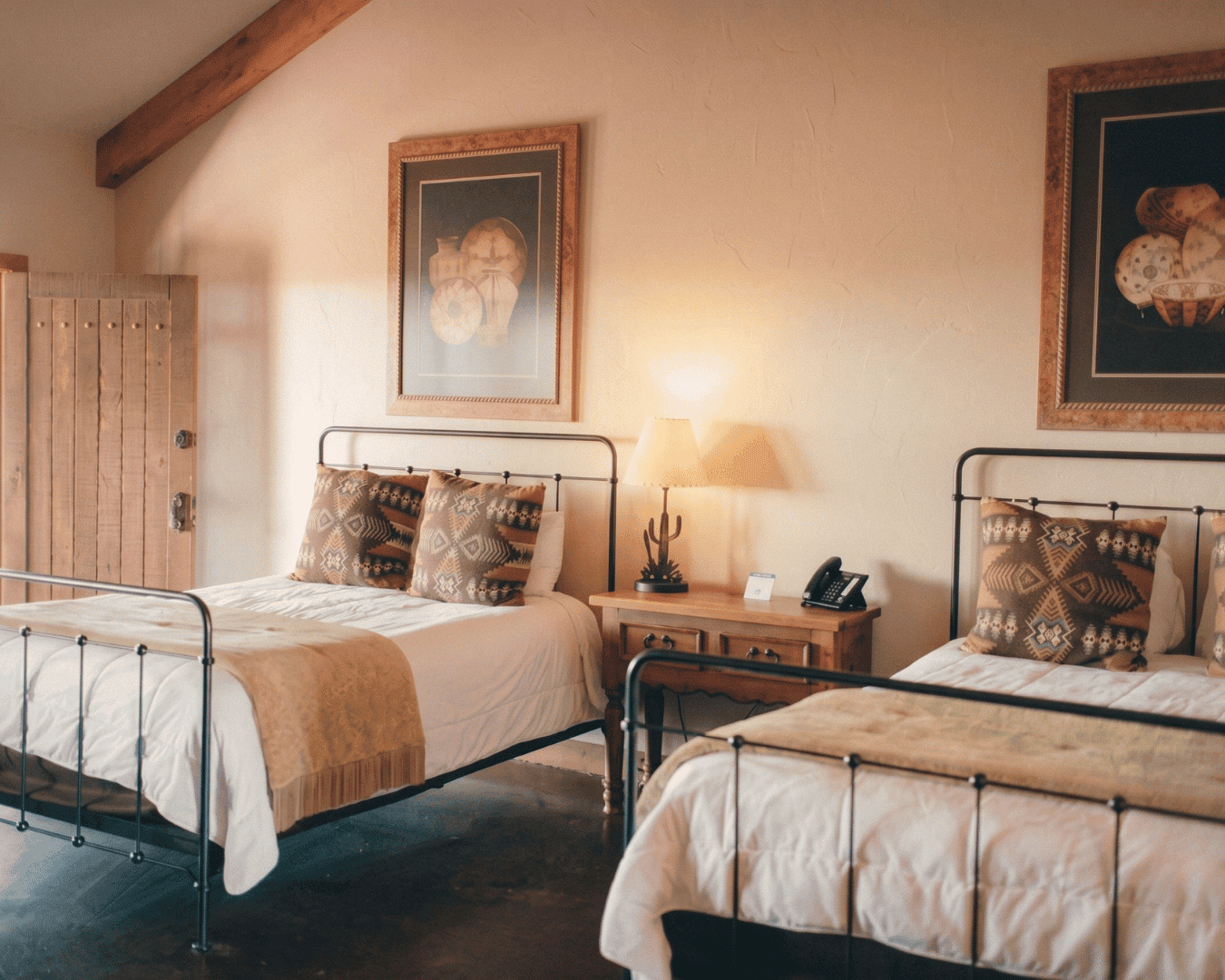 Rustic bedroom with two metal beds, artwork, and warm lighting.