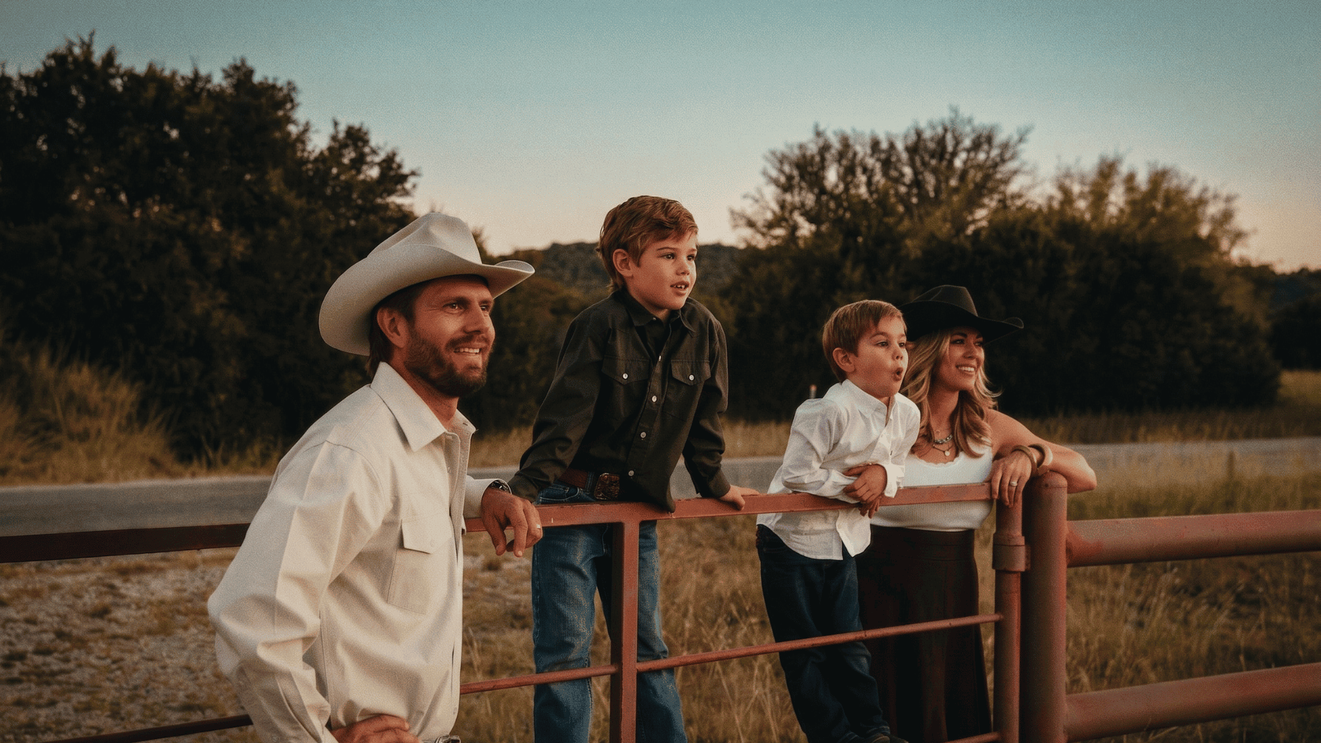 Family with children at sunset on a ranch fence, enjoying outdoor time.
