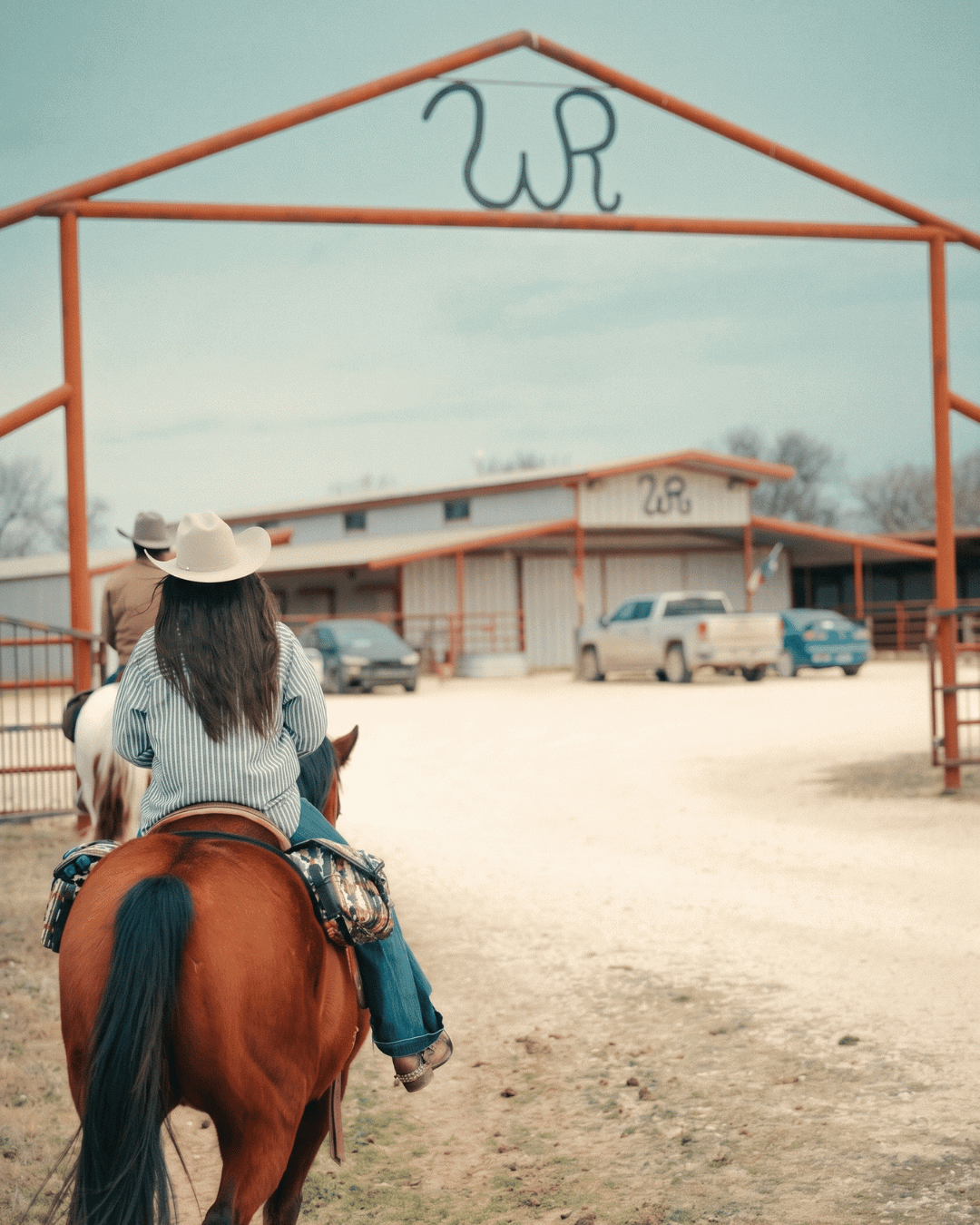 Person riding a horse towards a ranch entrance with WP logo.