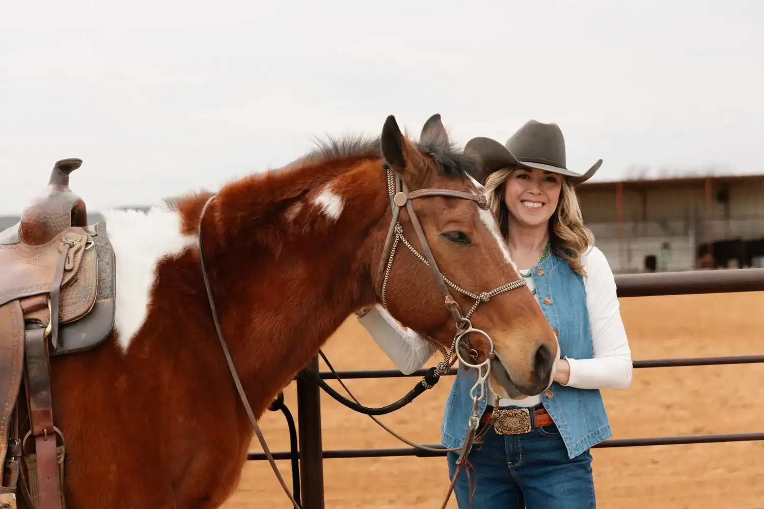 Happy woman with cowboy hat and horse at ranch.