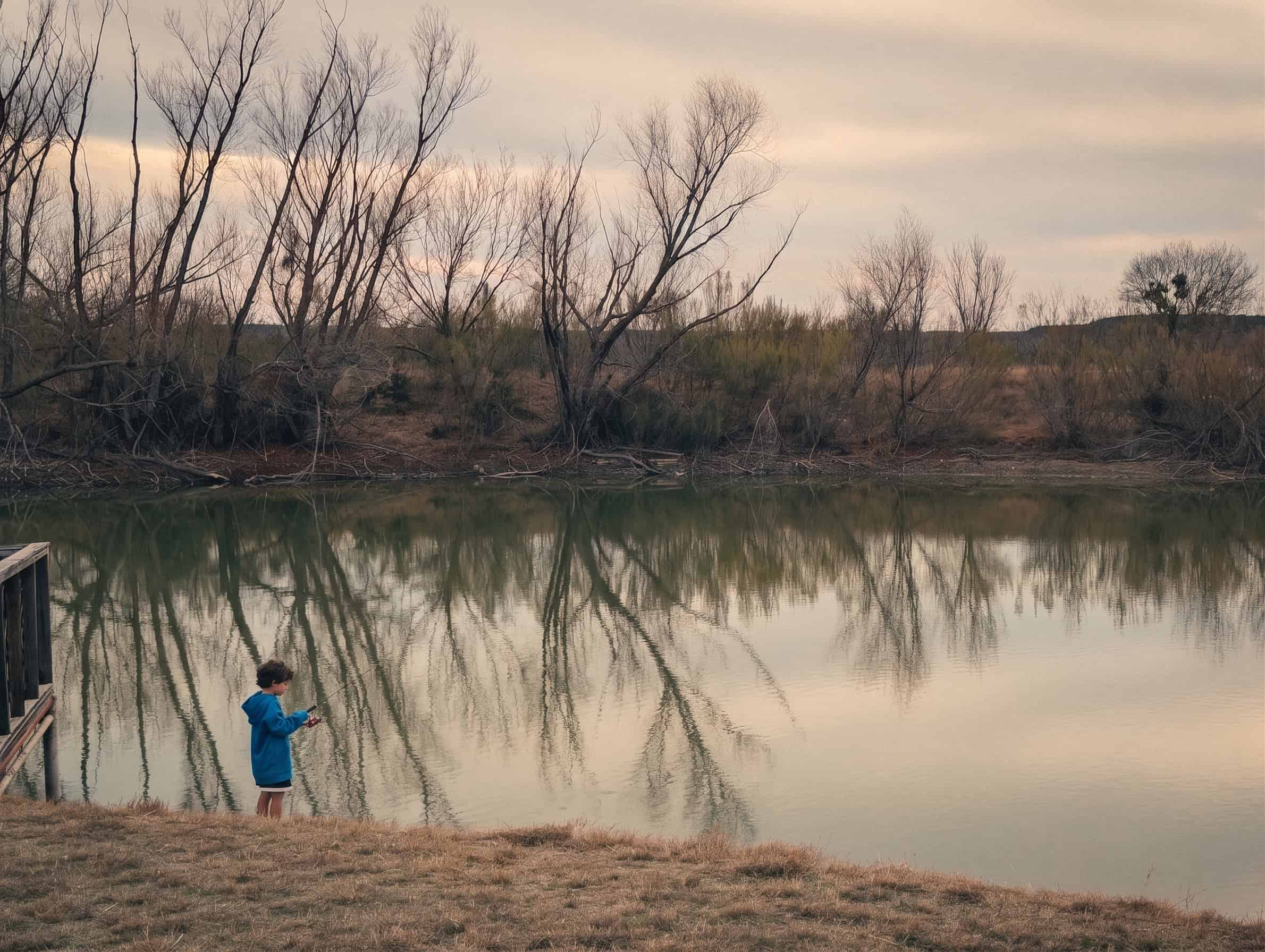 Child fishing by the pond at Wildcatter Ranch during sunset.