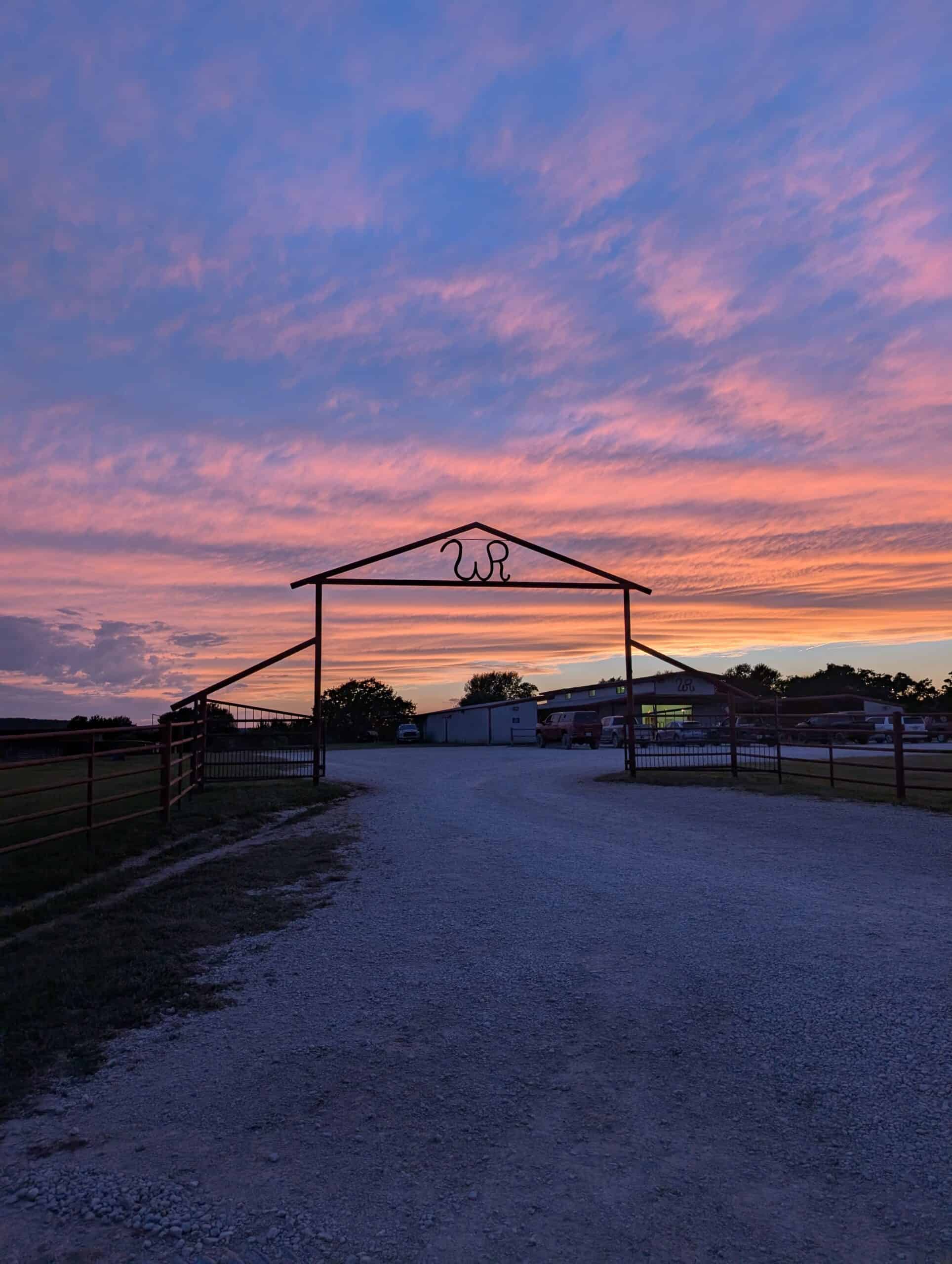 Scenic sunset view at Wildcatter Ranch entrance with colorful sky and rustic gate.