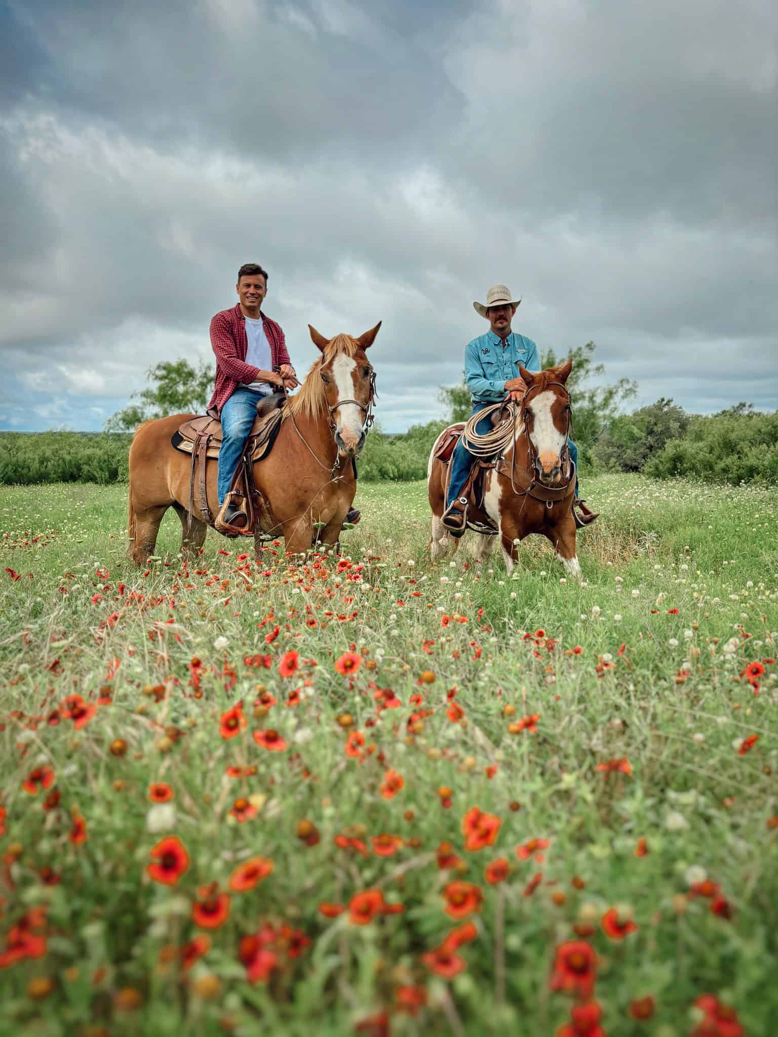 Two men riding horses in a field of wildflowers at Wildcatter Ranch.