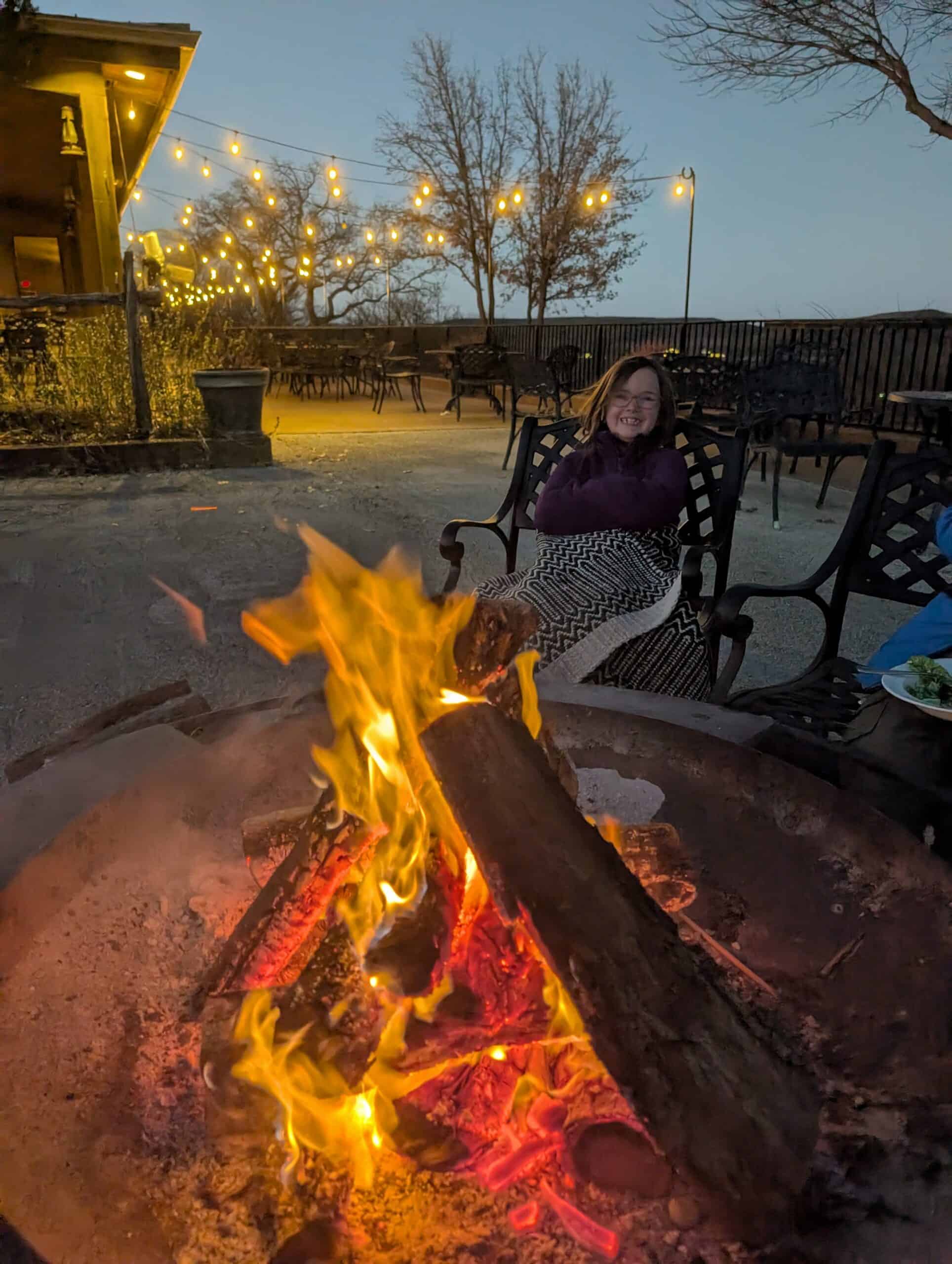 Woman enjoying outdoor firepit at Wildcatter Ranch with string lights overhead.